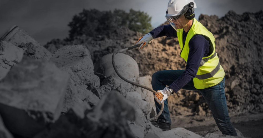 A man wearing an industrial safety hardhad, vest, gloves, and hearing protection.