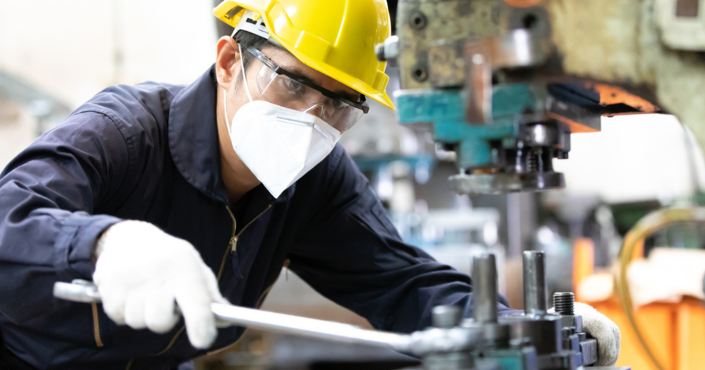 Man wearing a safety breathing mask while operating an industrial machine.