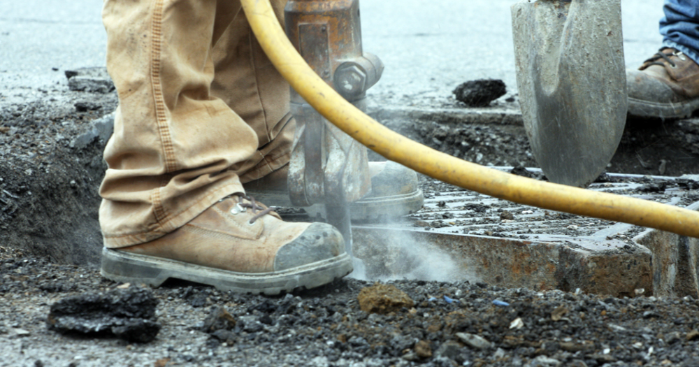 An industrial worker operating a jackhammar wearing steel toe safety boots.