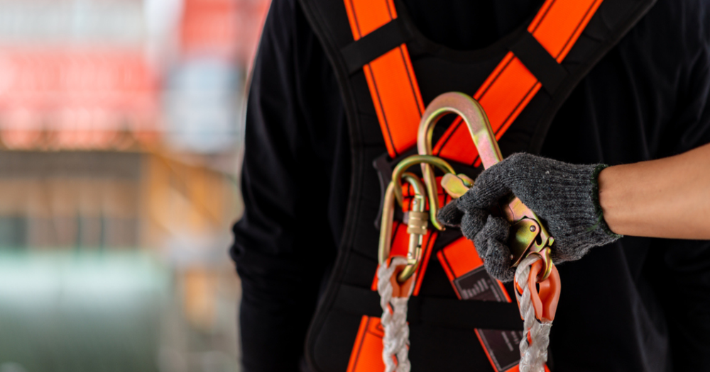 An industrial worker putting on a fall safety harness with lead rope.