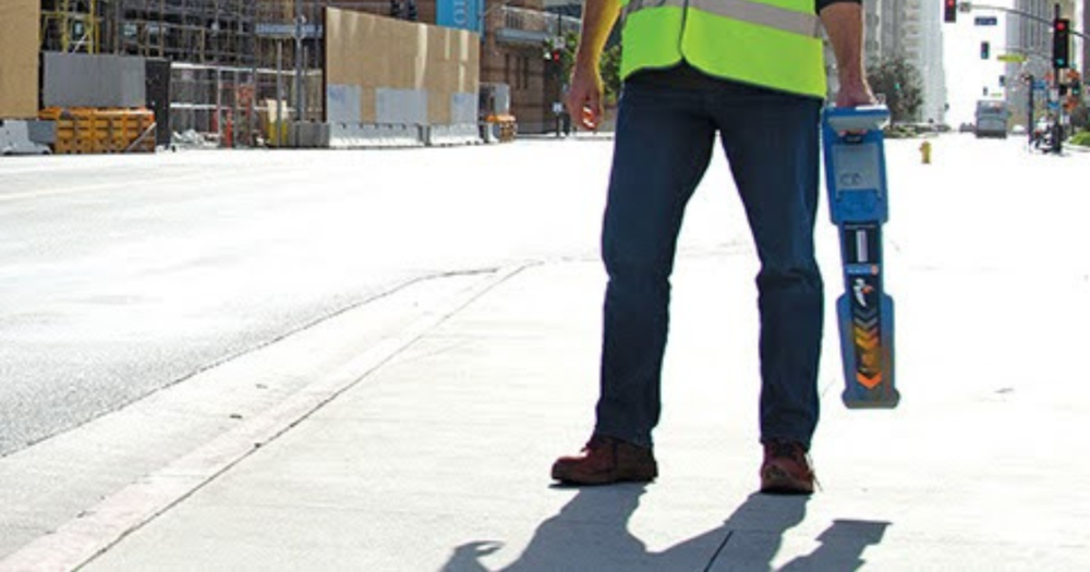 A man using a magnetic locator on the sidewalk for a construction project.