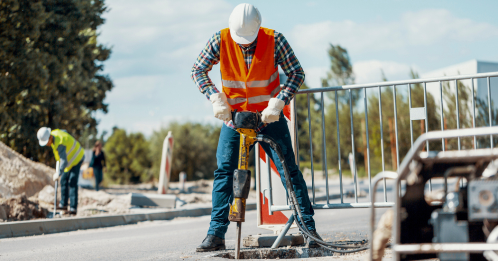 A man wearing an orange safety vest using a jackhammer.