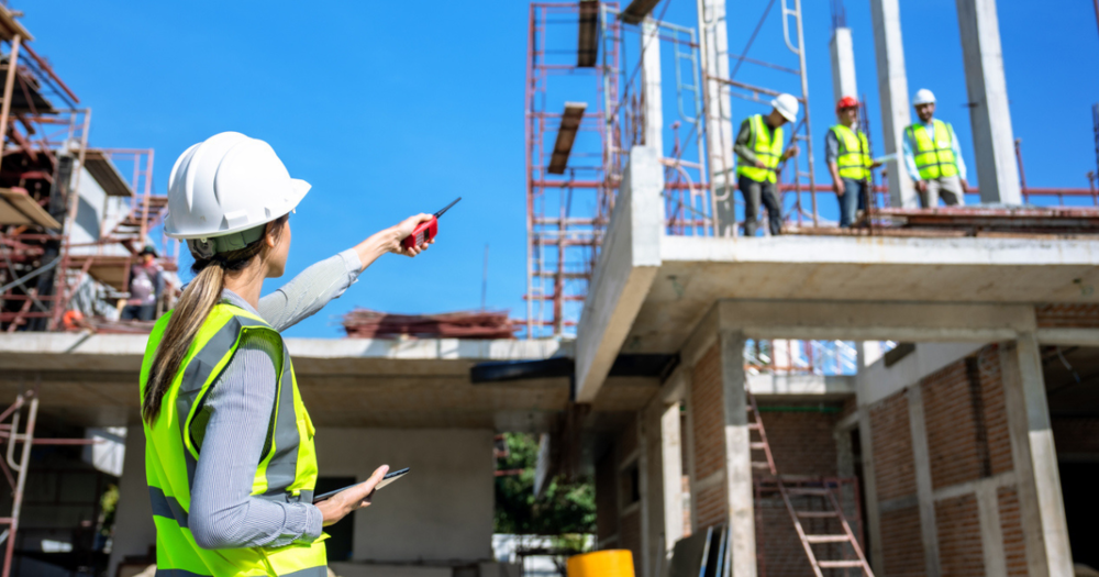 A woman construction supervisor in a yellow safety vest giving instructions to other construction workers.