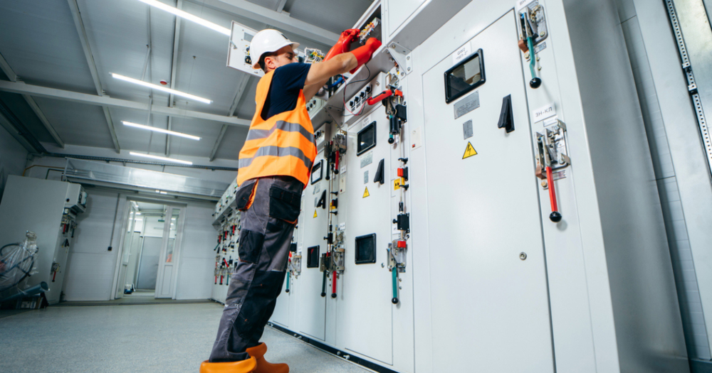 An electrician in an orange safety vest working on a breaker.