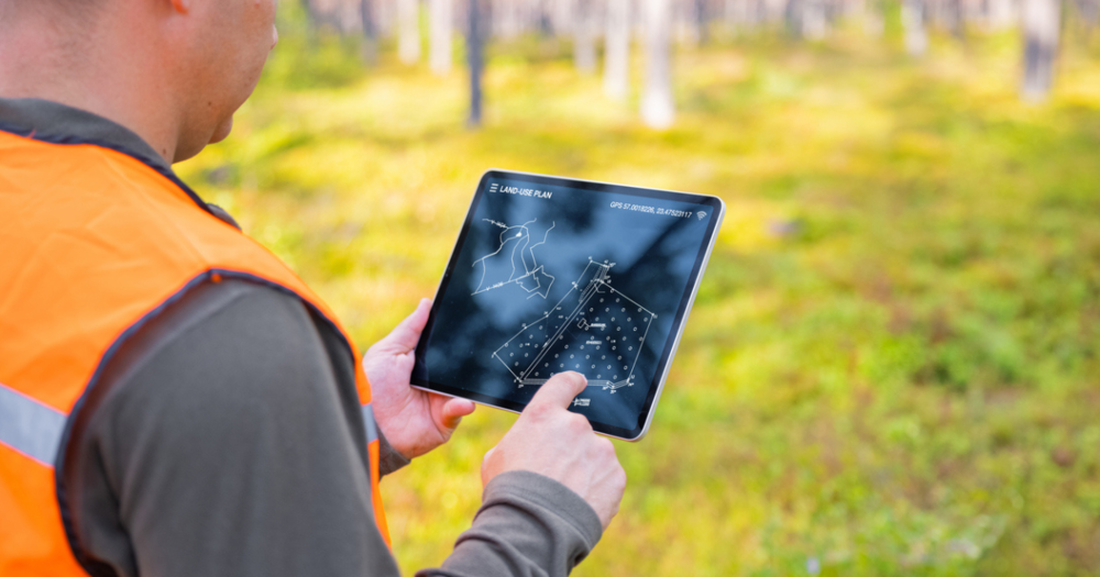 A man using a handheld gps unit to land survey a forest.