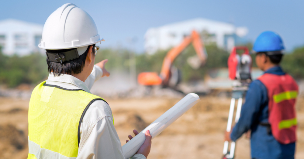 Two men at a construction site using a total station for a land survey.