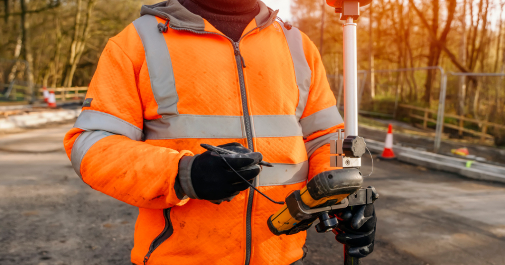 A man using GPS equipment to conduct a land survey on a road.