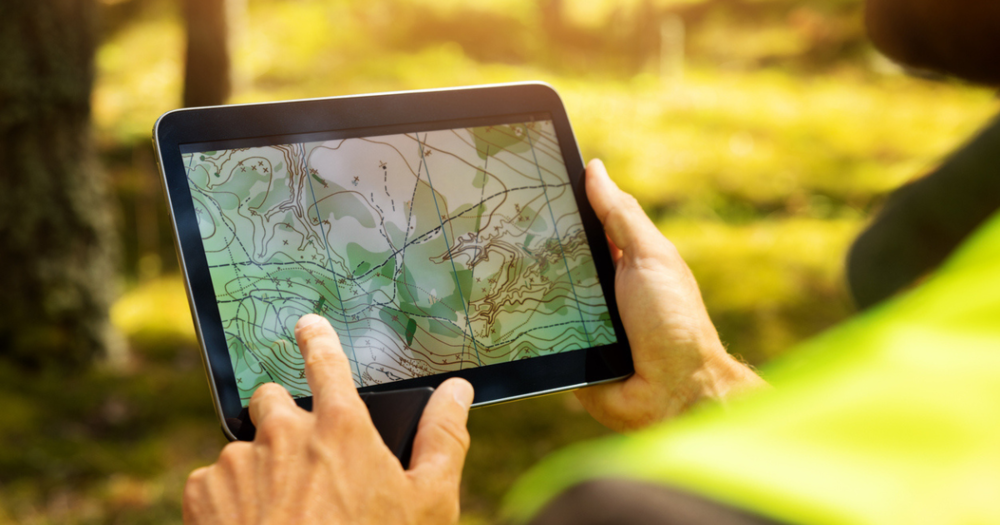 A person using a tablet to look at a GPS land survey map of a forested area.