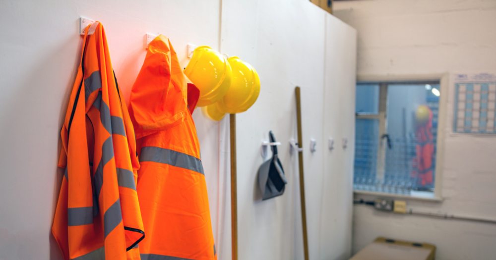 Several safety vests and hard hats organized on a wall hook.